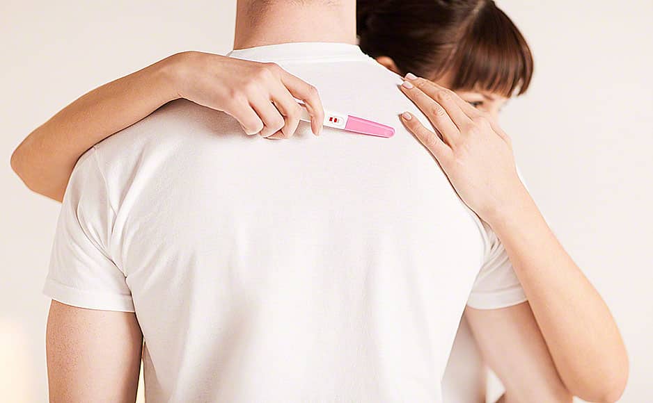 20112279 – close up of woman with pregnancy test hugging man