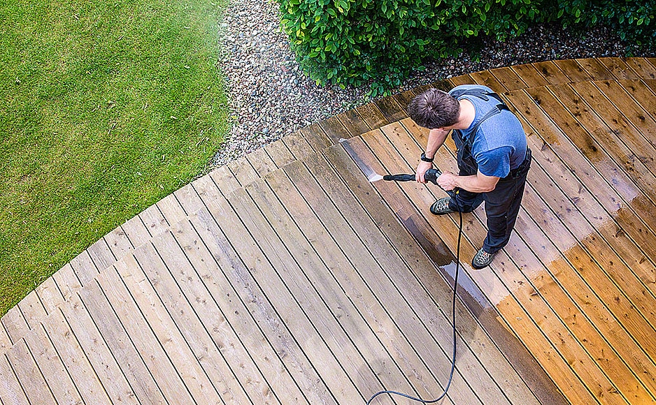 man cleaning terrace with a power washer – high water pressure cleaner on wooden terrace surface