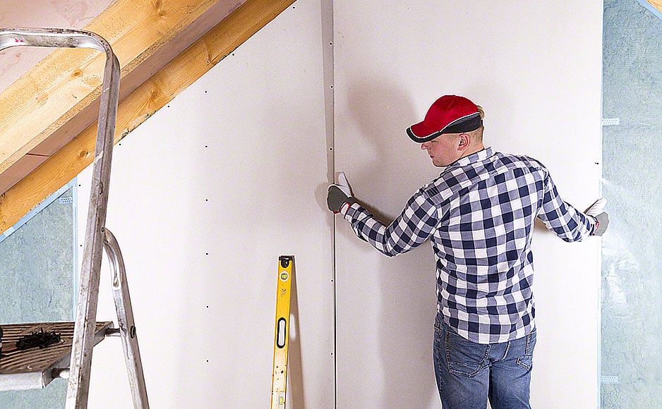 Construction worker holding gypsum board. Attic renovation. Installation of drywall