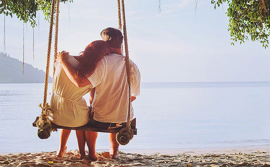 romantic holidays, honeymoon, affectionate couple on beach on swing