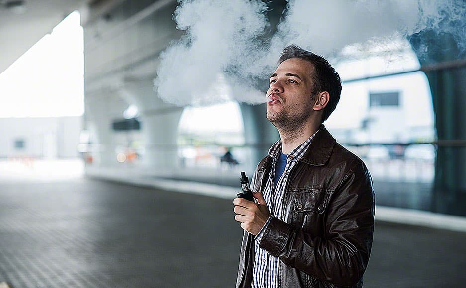 Young traveller man smoking an electronic cigarette outdoor near the airport terminal